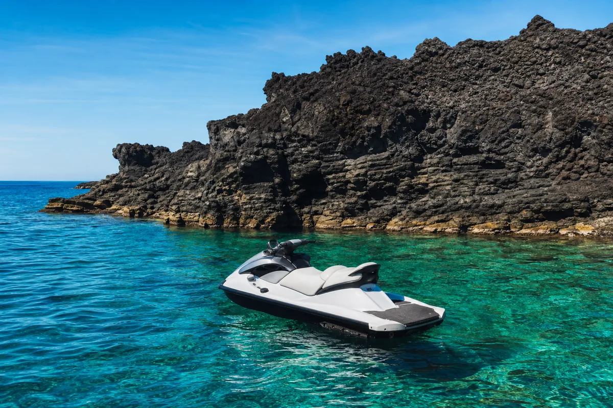 Jet-ski a l&rsquo;arret dans une eau turquoise devant une falaise volcanique sombre